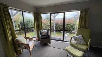 A room with large windows, a wicker chair, a cushioned armchair, and a small table.