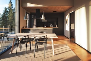 A modern kitchen with a dining area, large windows, and a view of trees.