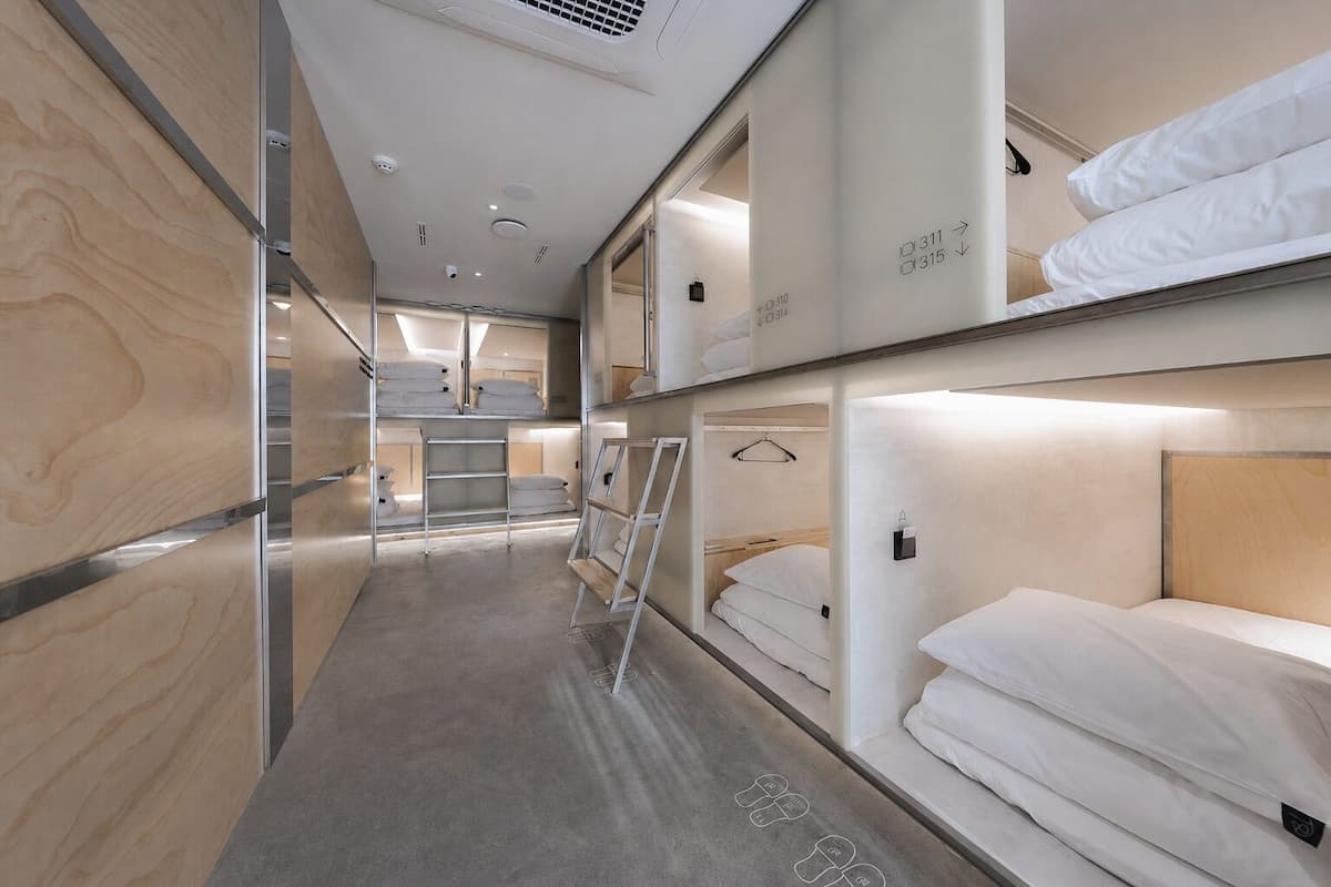 A modern train compartment with bunk beds, a central aisle, and a small seating area.