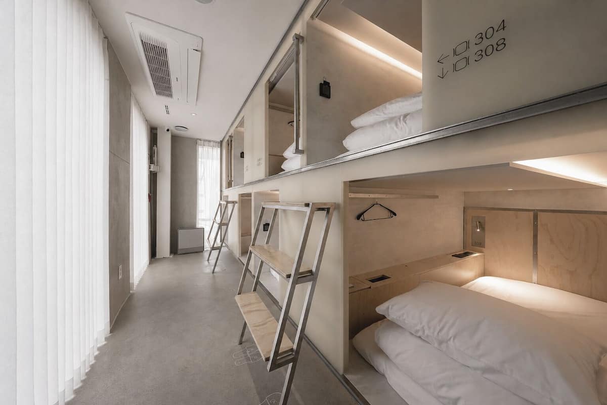 A hotel room with bunk beds, a ladder, a bedside table, a hanging light, and a mirror.