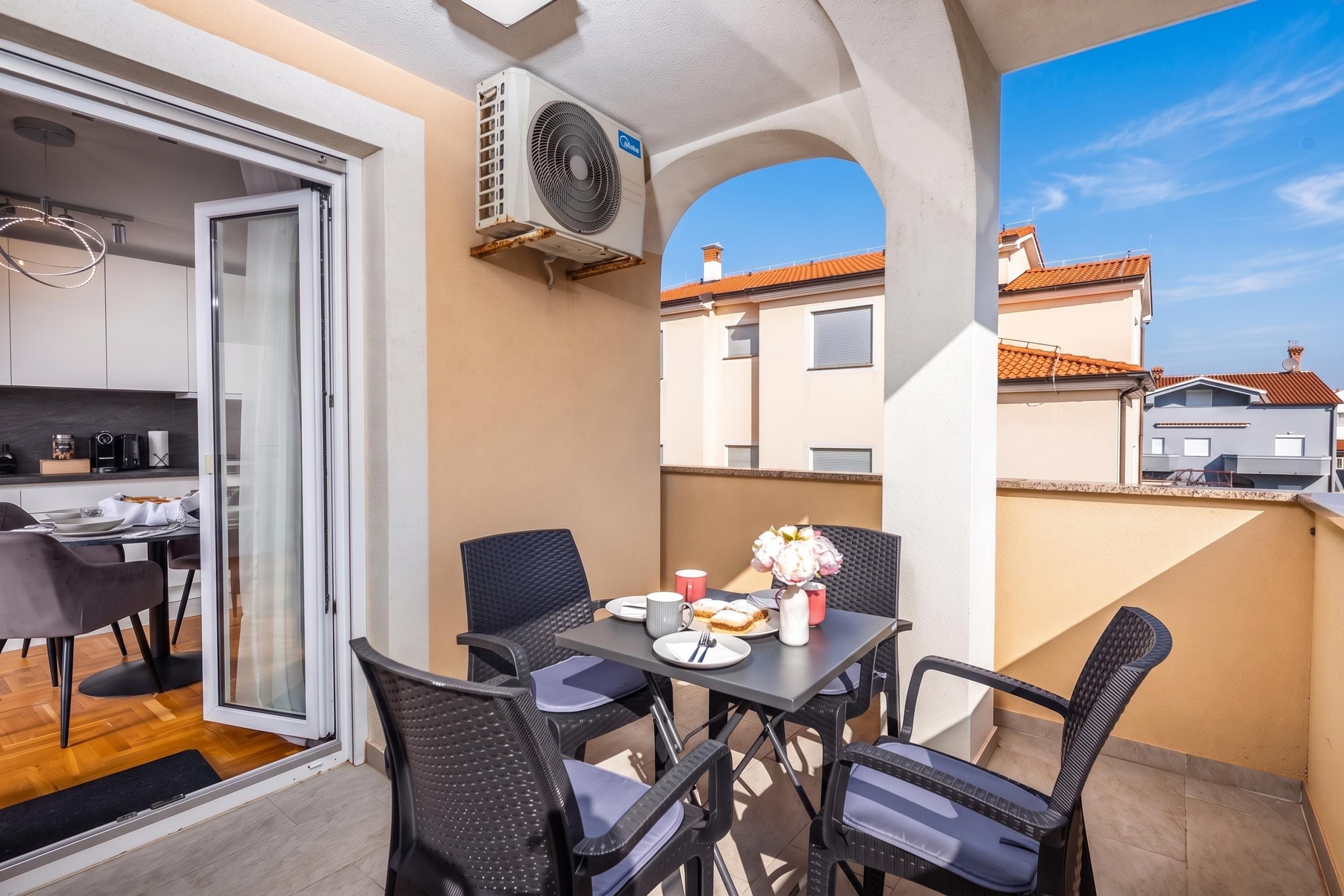 A balcony with a dining table, chairs, and a fan.