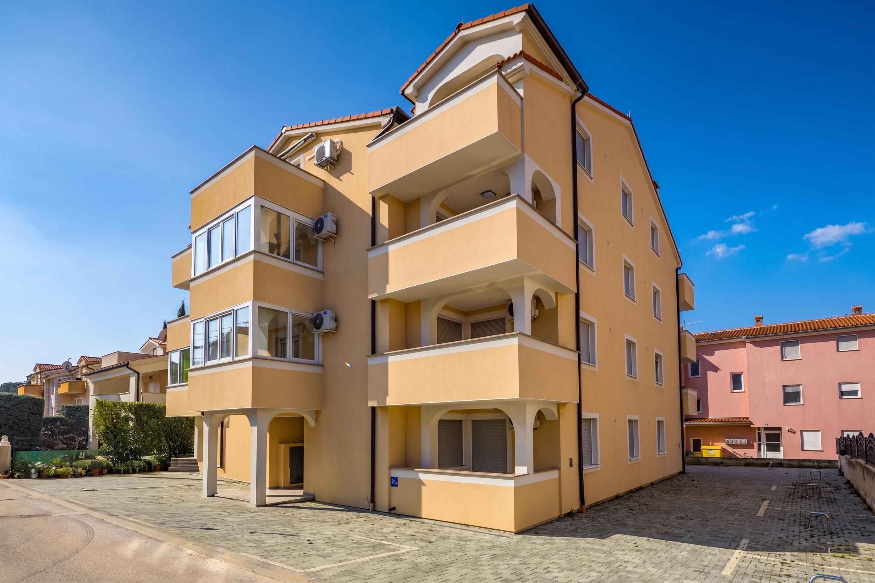 A multi-story residential building with balconies, air conditioning units, and a paved courtyard.