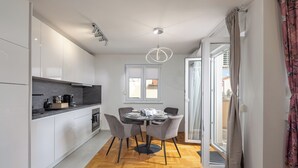 A modern kitchen with white cabinets, a black countertop, and a dining area with a round table and four chairs. - Apt Ana Walk To Beach /w Balcony (Medulin)