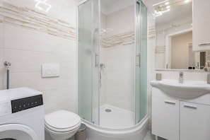 A modern bathroom with a glass-enclosed shower, a toilet, a washing machine, and a sink with a mirror. - Apt Ana Walk To Beach /w Balcony (Medulin)