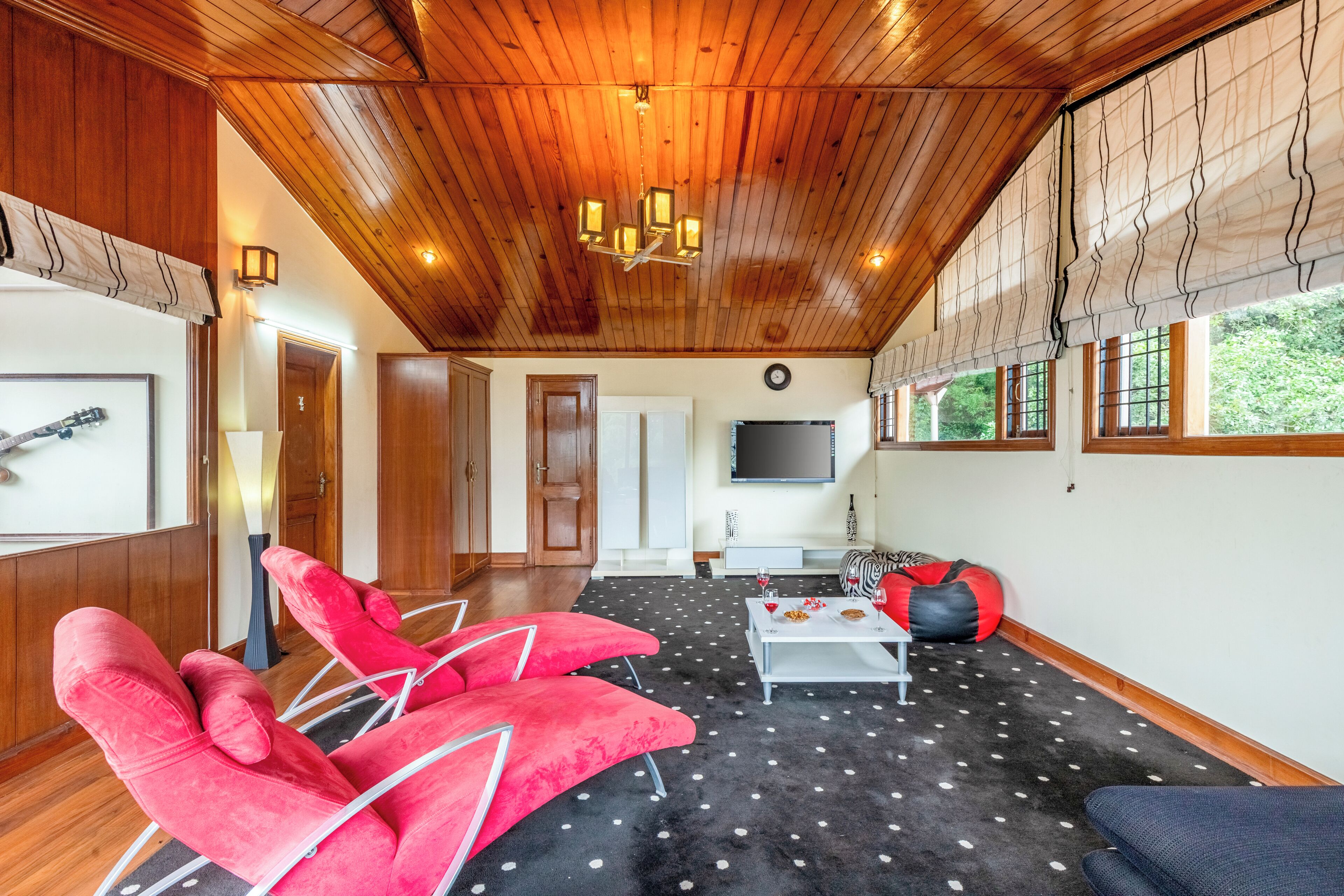 A spacious living area with a wooden ceiling, a flat-screen TV, red chairs, a coffee table, and a patterned carpet.