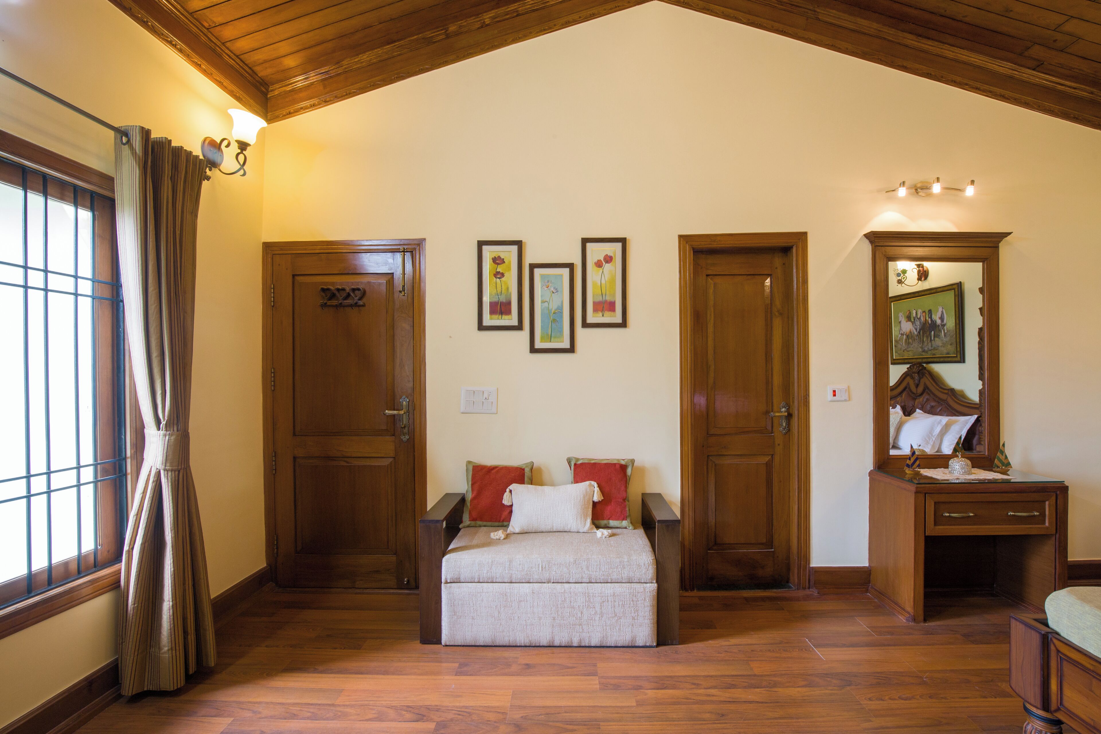 A room with a bed, a desk, and a mirror. There are three framed pictures on the wall.