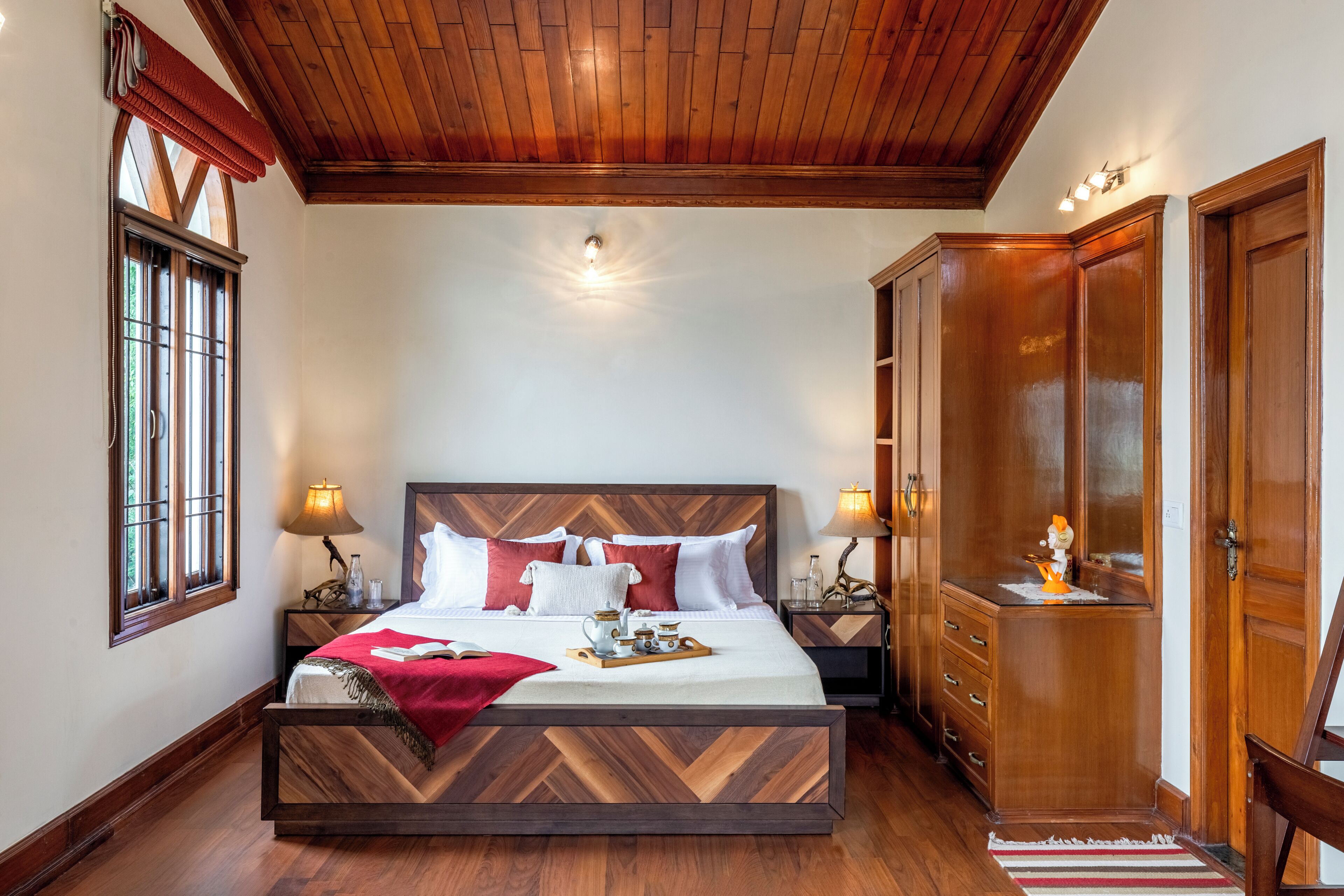 Un dormitorio con cabecera de madera, una cama grande, mesitas de noche con lámparas, un armario y una ventana con cortinas.