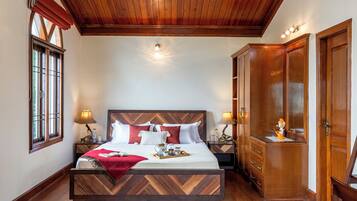 Un dormitorio con cabecera de madera, una cama grande, mesitas de noche con lámparas, un armario y una ventana con cortinas.