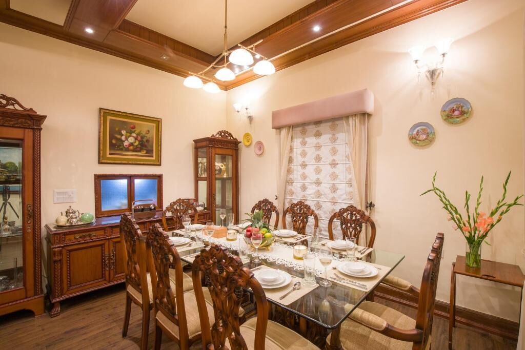 A dining room with a glass table, wooden chairs, a cabinet, and wall-mounted light fixtures.