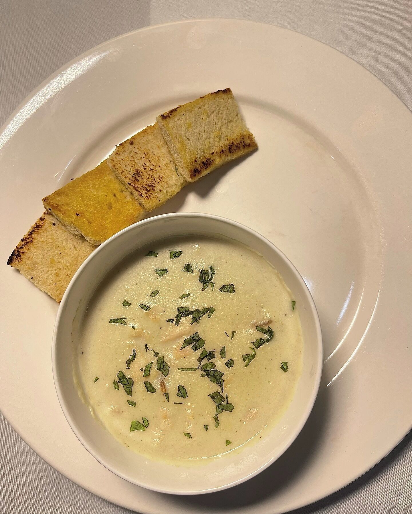 A bowl of creamy soup garnished with herbs, accompanied by toasted bread slices on a white plate.