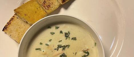 A bowl of creamy soup garnished with herbs, accompanied by toasted bread slices on a white plate.