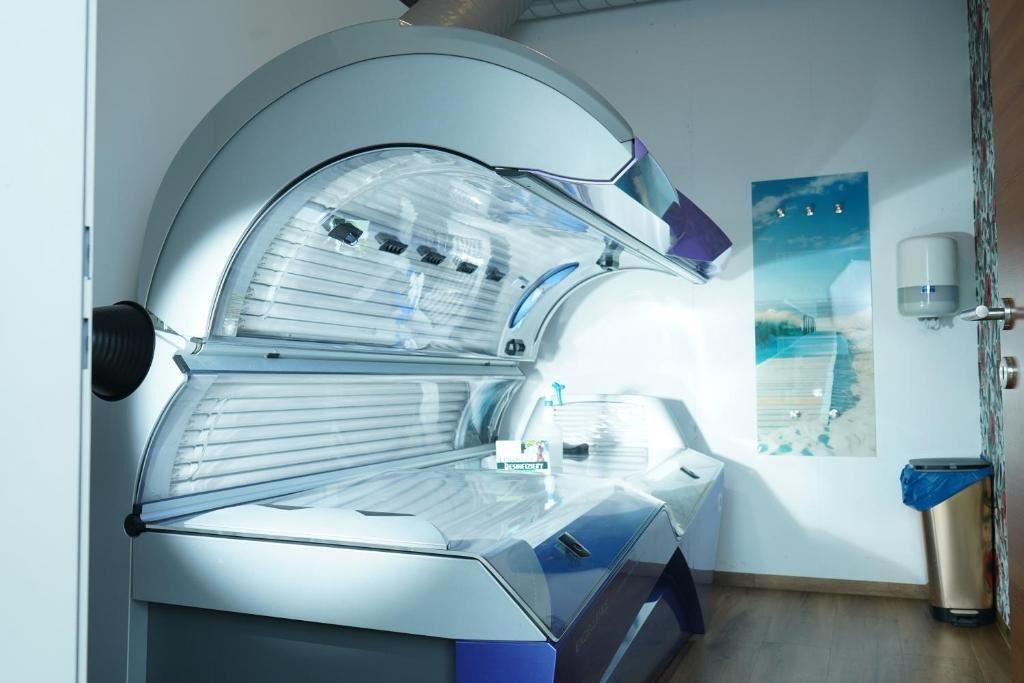 A tanning bed with a control panel, a trash bin, and a poster on the wall.