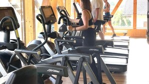 Kuntosali, jossa on juoksumattoja ja crosstrainereita, puuseinät ja suuret ikkunat.