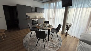 Moderni olohuone, jossa on pyöreä ruokapöytä, tummat tuolit, seinälle asennettu taulutelevisio ja taustalla keittiö.
