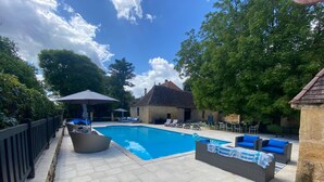 A swimming pool with lounge chairs and umbrellas, surrounded by stone buildings and trees. - Spacious 6-bedroom house in  Varennes, pool, 3 outdoor spaces, full gym, bikes. (Varennes)