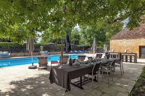 Un área de piscina al aire libre con sillones, una mesa de comedor y sombrillas.