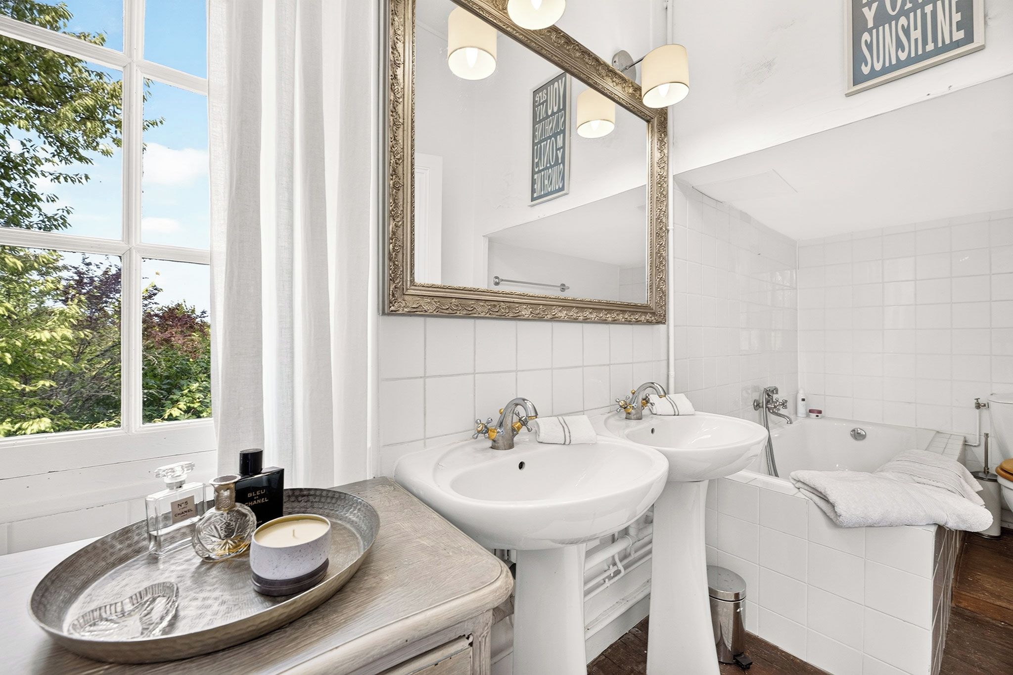 Une salle de bain avec deux lavabos, un grand miroir et une fenêtre avec des rideaux.