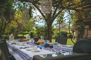 An outdoor dining area with a table set for two, surrounded by greenery and trees.
