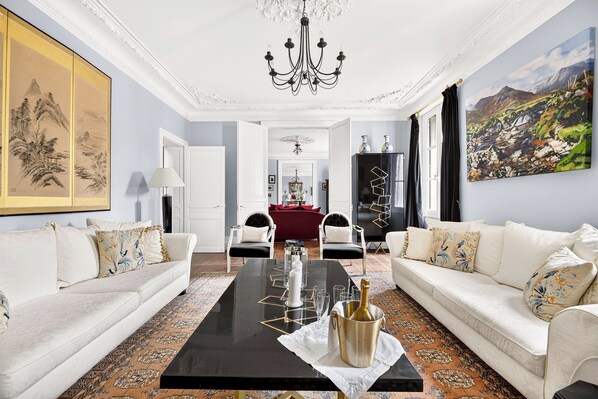 Un salón amplio con una mesa de centro negra, sofás blancos y un candelabro.