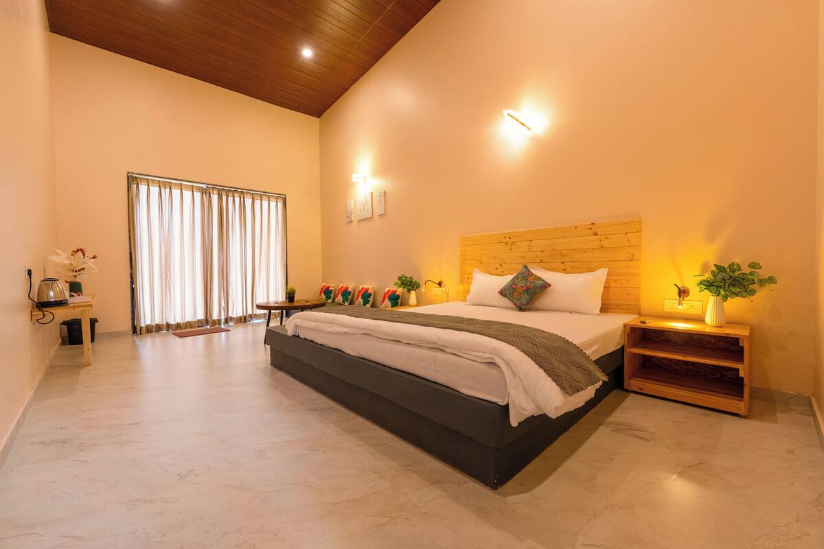 Un dormitorio con una cama grande, mesitas de noche, un tocador, una ventana con cortinas y un techo de madera.