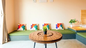Una habitación con un banco acolchado verde, una mesa redonda de madera con una planta, y una pared decorada con tres obras de arte enmarcadas.