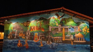 Un mural en la fachada de un edificio que representa diversos elementos culturales e históricos, incluyendo un templo, una fábrica y un faro.
