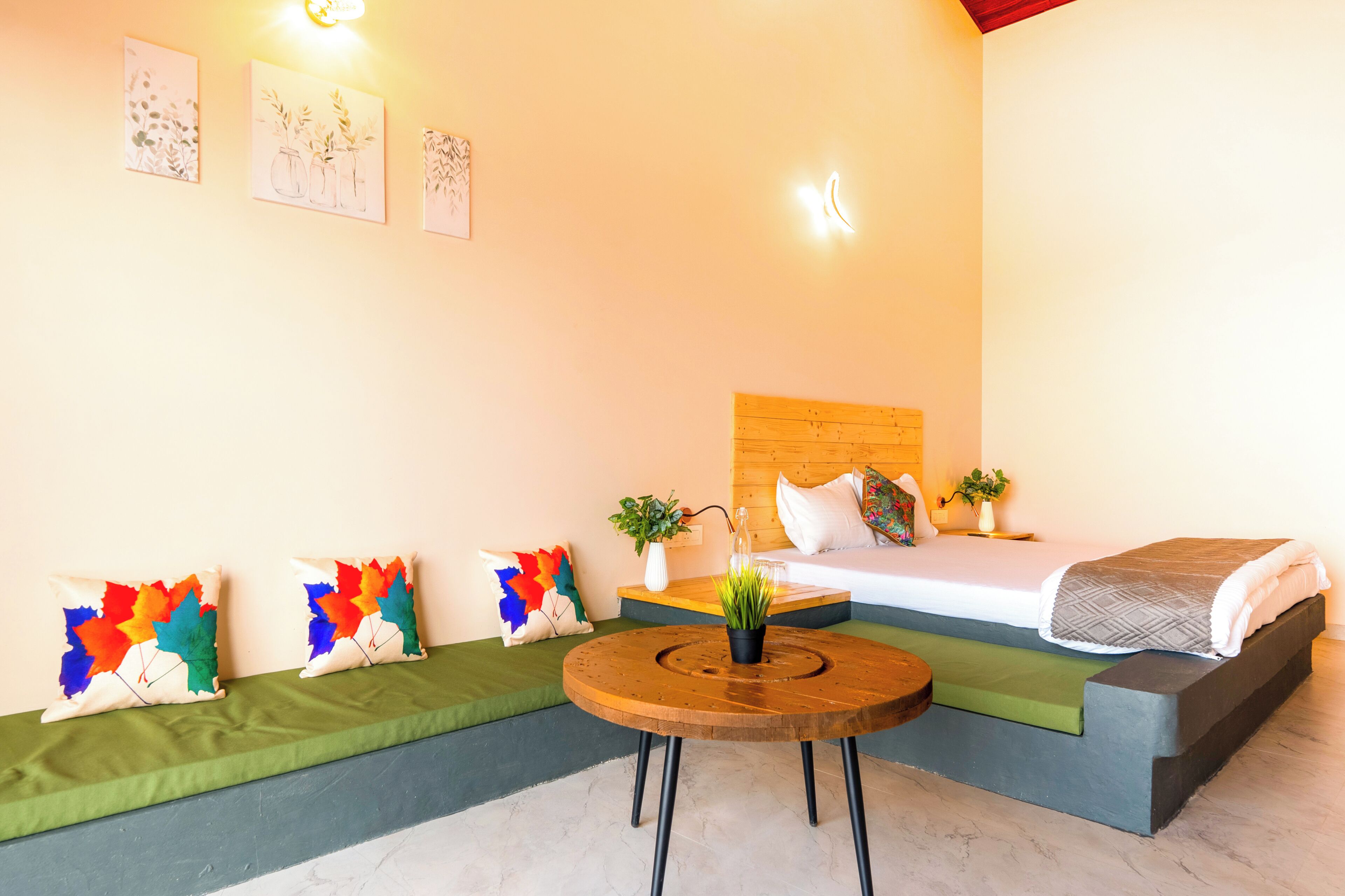 A room with a bed, a round wooden table, a green sofa, and a small plant.