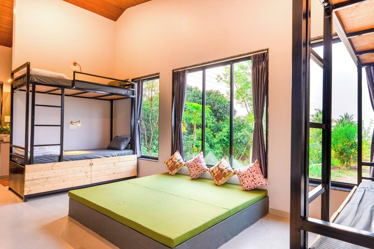 Una habitación con literas, un colchón verde y ventanas grandes con cortinas.