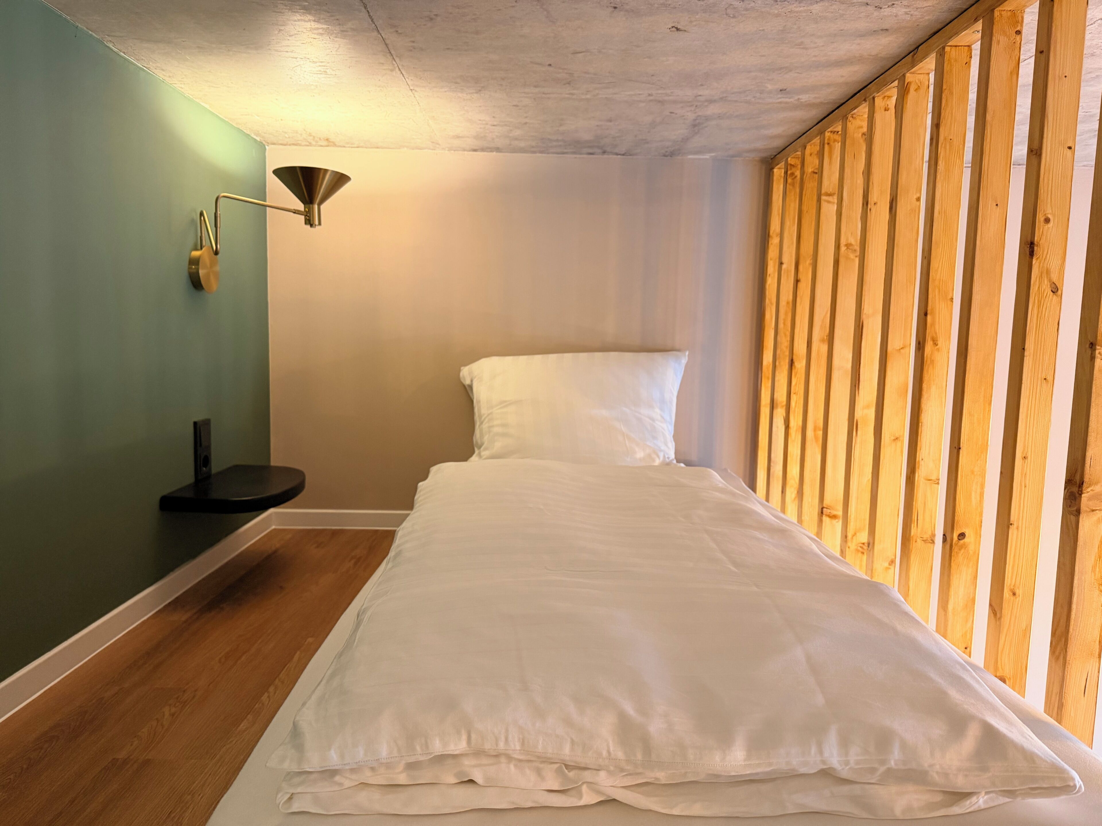 Ein Schlafzimmer mit einem Bett, einem Nachttisch, einer Lampe und Holzlamellen an einer Wand.