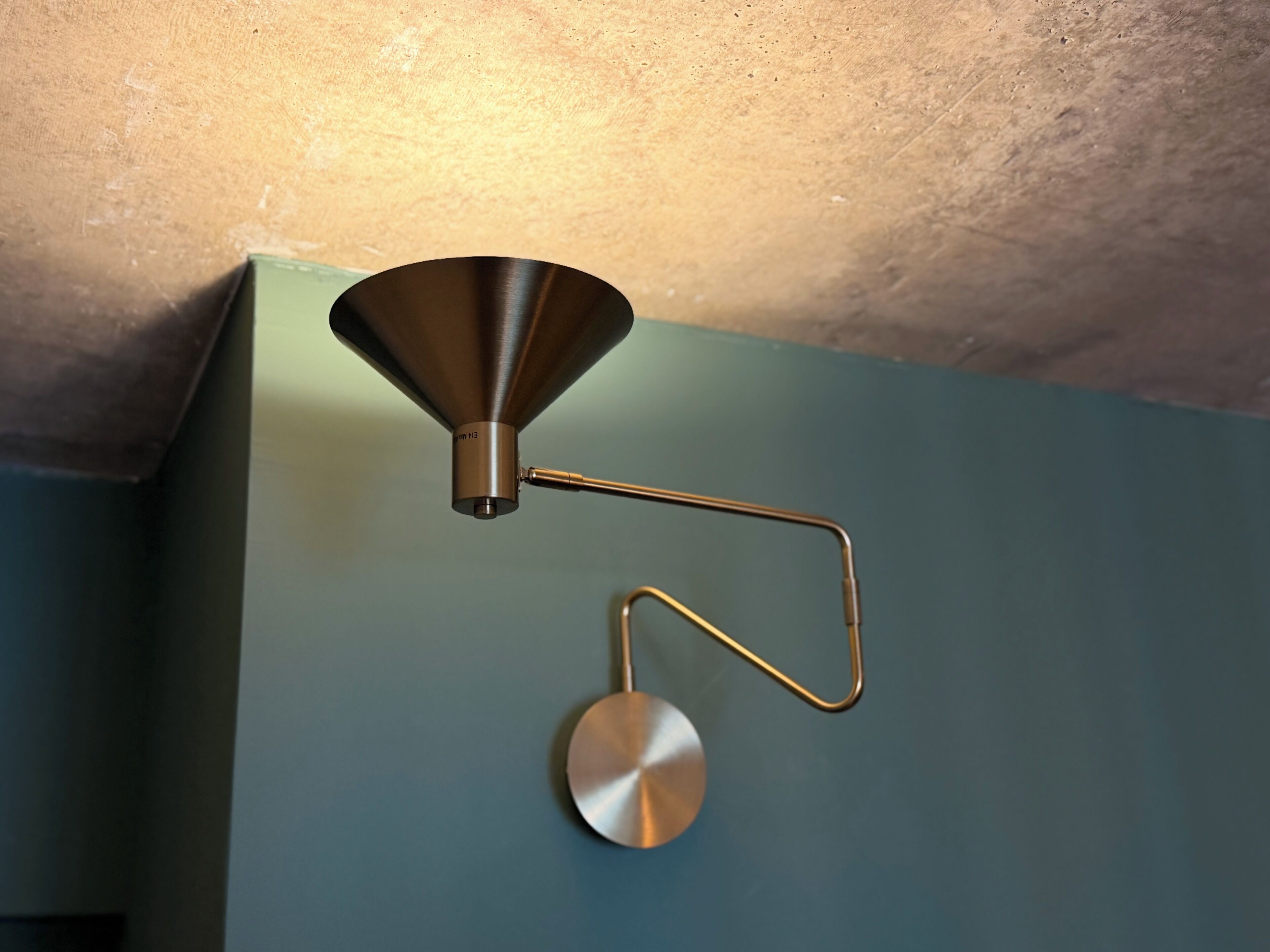 A wall-mounted light fixture with a conical shade and a circular base.