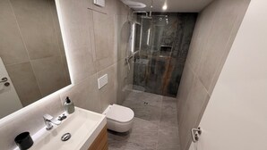 Een moderne badkamer met een wit wastafelmeubel, een douche met glazen wanden en een toilet.