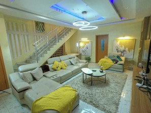 A living room with a sofa, coffee table, and a staircase. - ELORAH HOMES (Lekki)