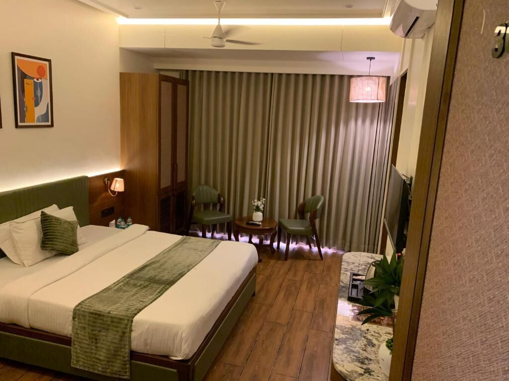 A hotel room with a bed, a desk, a chair, a small table, and a curtain.