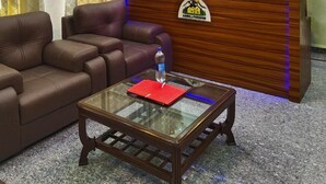 A reception area with a wooden desk, leather sofa, and a glass coffee table. - AASRA PARADISE HOTEL (Dharamshala)