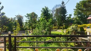A gated area with a metal fence and decorative elements, surrounded by lush greenery and trees. - AASRA PARADISE HOTEL (Dharamshala)