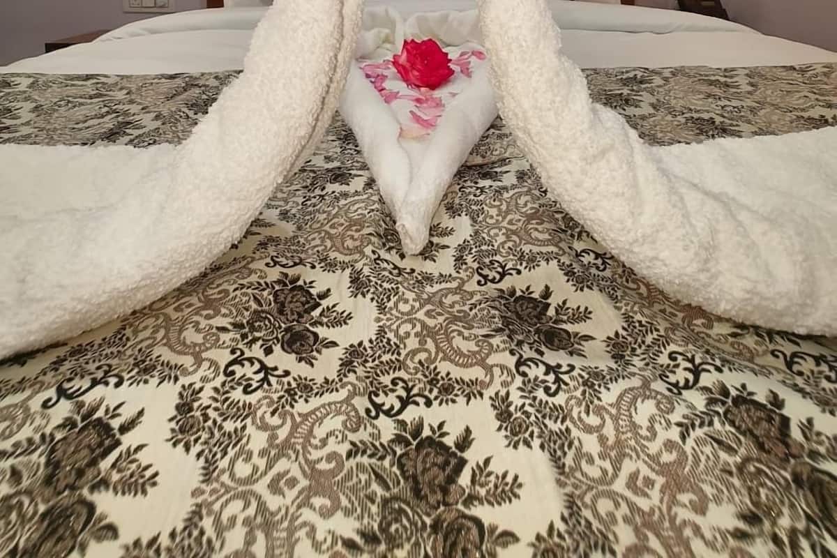 A bedroom with a bed, a heart-shaped towel arrangement, a single red rose, and a painting on the wall.