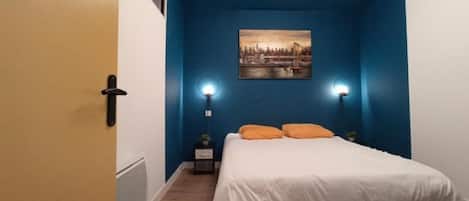 Een slaapkamer met een bed, twee bedlampen, een nachtkastje, een schilderij aan de muur en een deur.