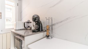 Una cocina con cafetera, tostadora y un recipiente de vidrio transparente en la encimera.