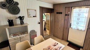Een kamer met een houten deur, een tafel met een krant, een plank met keukengerei en een wandklok.
