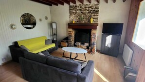 Een woonkamer met een bank, een ronde tafel, een open haard en een televisie.