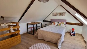 Een slaapkamer met een schuine kap, een bed met beddengoed met een patroon, een kleine tafel, een stoel en een decoratief wandobject.