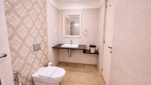 Uma casa de banho com sanita, lavatório, espelho e porta-toalhas.