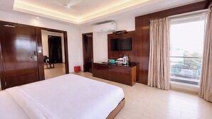 Quarto de hotel com uma cama grande, uma televisão de tela plana na parede, cômoda e uma janela com cortinas.