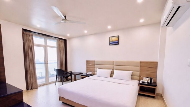 Quarto de hotel com cama, escrivaninha, cadeira, mesa de cabeceira e ventilador de teto.