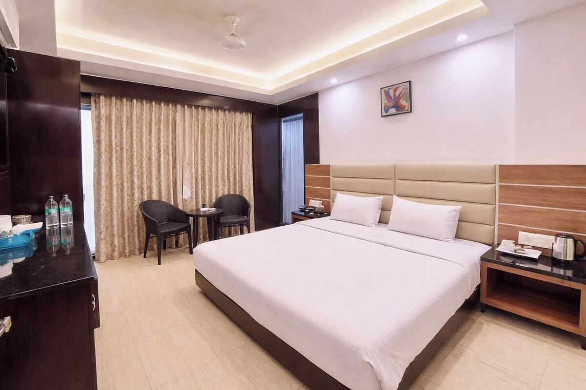 A hotel room with a large bed, a desk with a telephone, two chairs, a coffee maker, and a painting on the wall.