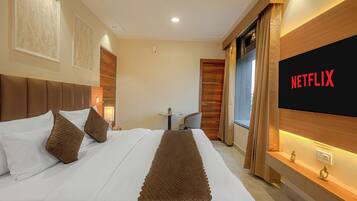 A hotel room with a bed, a TV mounted on the wall, a ceiling fan, and a small table with a chair.