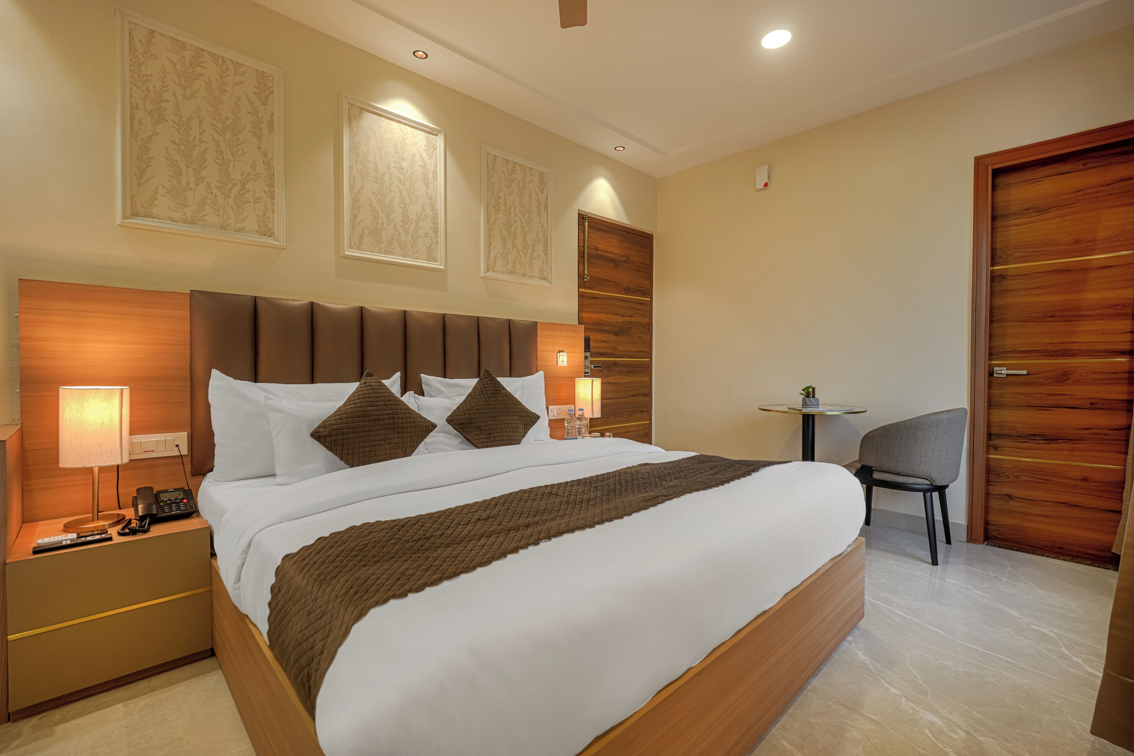 A hotel room with a large bed, bedside tables, a small table, a chair, and a wooden door.