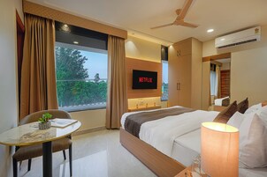 Habitación de hotel con cama, televisor montado en la pared, ventilador de techo y ventana con cortinas.
