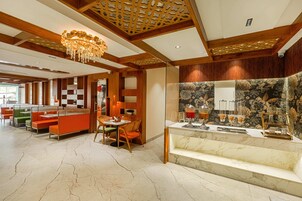 Un moderno vestíbulo de hotel con paneles de madera, una araña, un mostrador de recepción de mármol y una zona de estar con mesa y sillas.