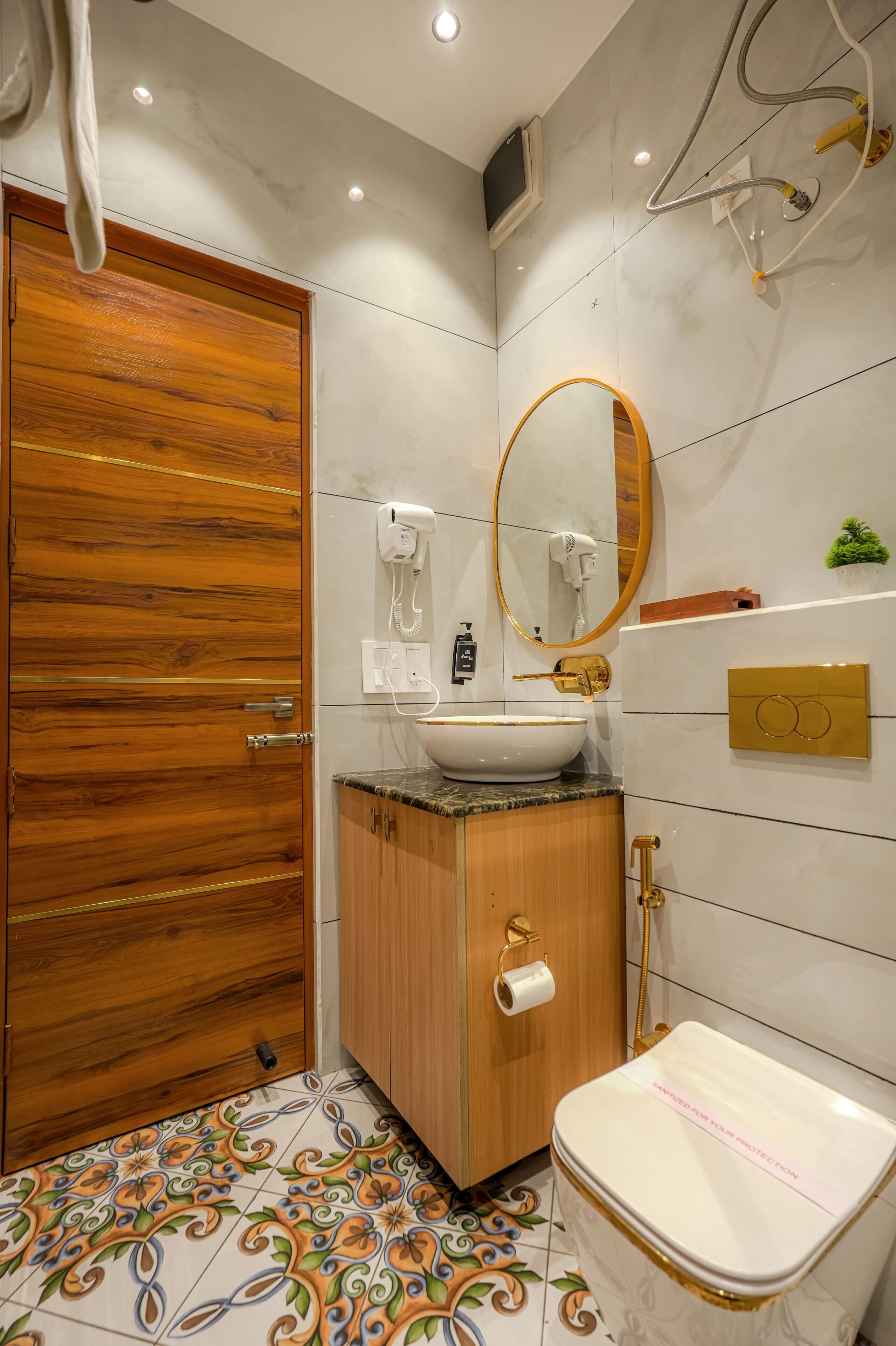 Un baño con puerta de madera, un lavamanos con grifo dorado, un inodoro y un espejo.